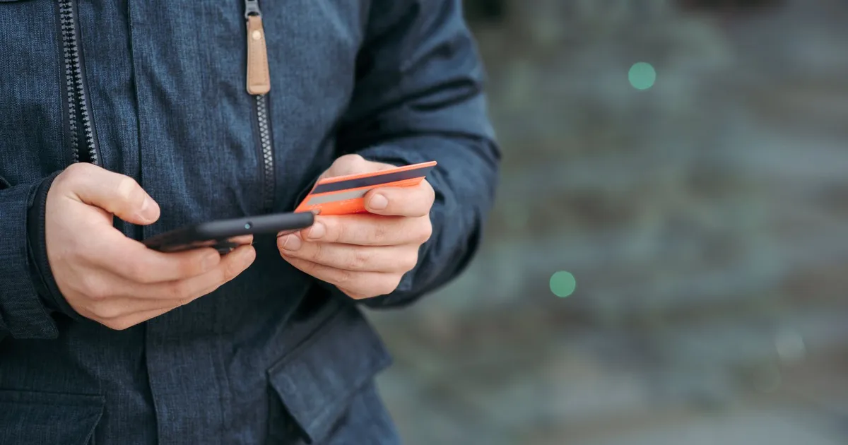 Kund som betalar ett köp på mobilen med ett betalkort i handen