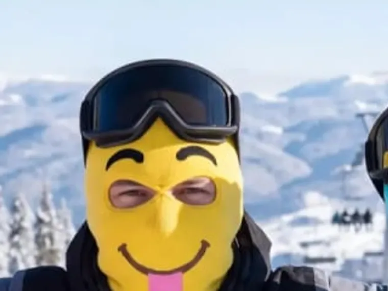 Derp — noggos gula stickade skidmask med smiley och tunga, i skidbacken.