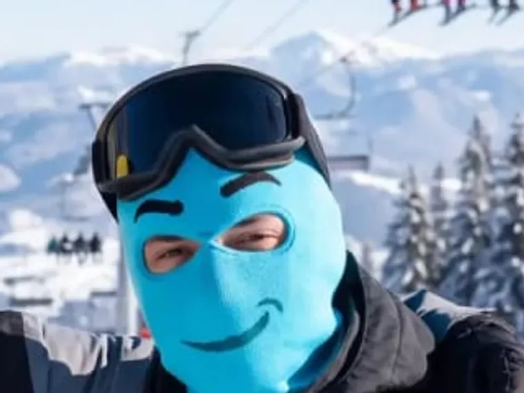 Grimm — noggos blå stickade skidmask med smil, i skidbacken.